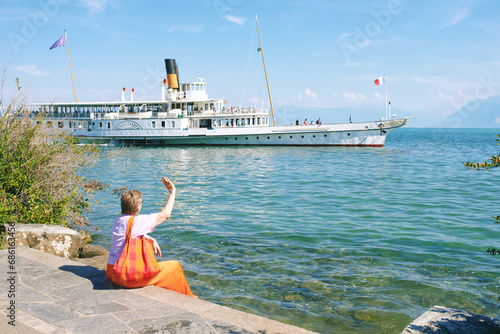 Outdoor portrait of mature 50 - 55 year old woman sitting by the lake, watching floating swiss french boat on lake Geneva, Switzerland © annanahabed