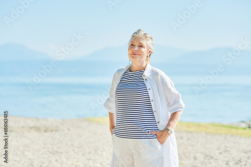 Outdoor summer portrait of happy and healthy mature 50 - 55 year old woman enjoying nice sunny day by the lake or sea, active lifestyle photo