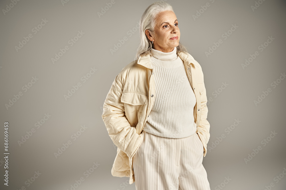 attractive and grey haired middle aged woman in trendy winter outfit posing with hands in pockets attractive and grey haired middle aged woman in trendy winter outfit posing with hands in pockets