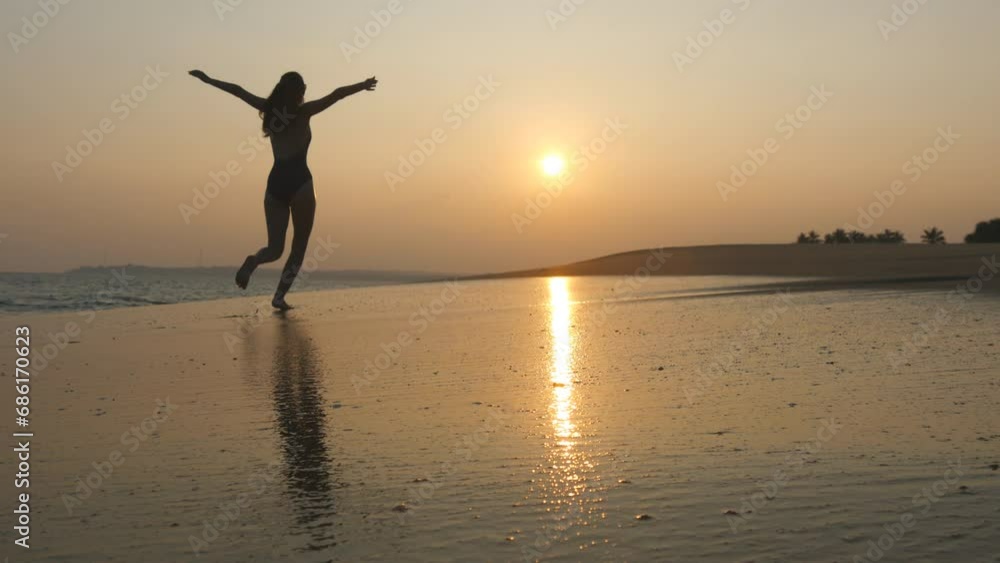 Young woman in swimsuit running on sand beach near ocean at sunset. Beautiful young girl jogging on sea shore with waves and enjoying vacation. Concept of relaxing on summer holiday. Slow motion Young woman in swimsuit running on sand beach near ocean at sunset. Beautiful young girl jogging on sea shore with waves and enjoying vacation. Concept of relaxing on summer holiday. Slow motion