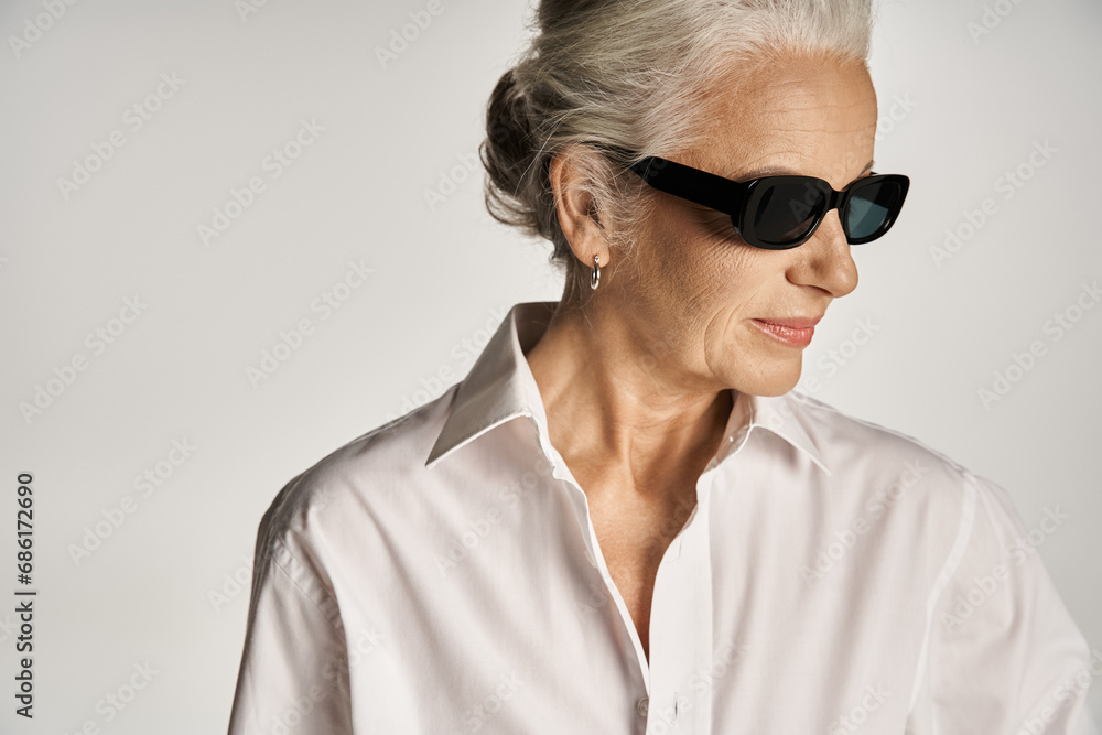 portrait of stylish middle aged woman in white shirt and sunglasses posing on grey background portrait of stylish middle aged woman in white shirt and sunglasses posing on grey background