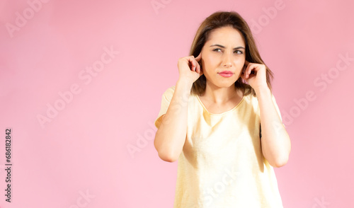 Image of a displeased young pretty blonde cute woman in casual t-shirt posing isolated over pink wall background covering ears because of loud.