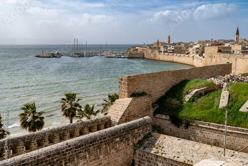 A fortified sea wall, a small boat harbor, mosque minarets and church towers all constructed from stone blocks, the old city of Acre, Israel