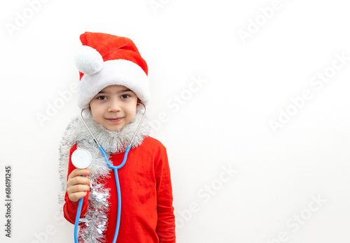 cute boy with santa claus cap and stethoscope playing with teddy bear,listening patient breathing,heartbeat.preschooler kid in red clothes with garland and tangerine covering eyes.candy cane as heart