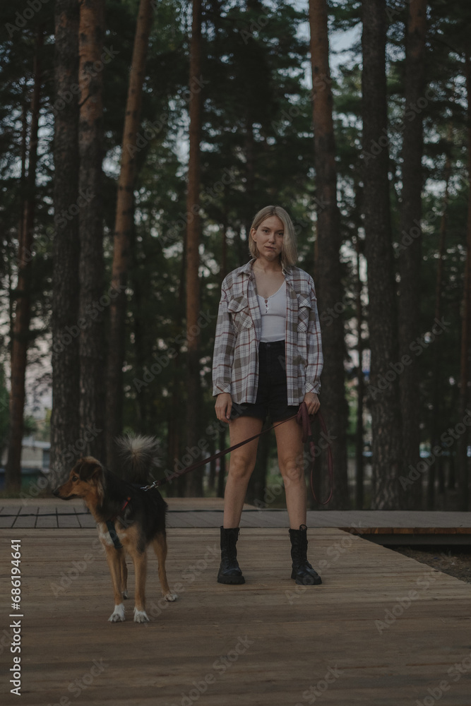 A young woman with her dog in a summer park. Happy girl walking in the woods with her mongrel dog. Concept of loving and helping dogs from a shelter. A young woman with her dog in a summer park. Happy girl walking in the woods with her mongrel dog. Concept of loving and helping dogs from a shelter.