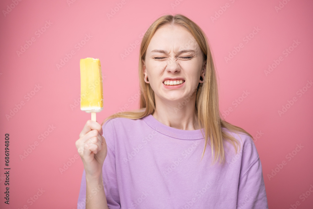 Happy young woman eating yellow ice cream on pink background. Concept of summer and sweet cold desserts. Happy young woman eating yellow ice cream on pink background. Concept of summer and sweet cold desserts.