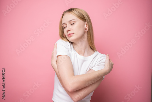 Cute girl smiling and hugging herself on pink background. Self-help and self-love concept
