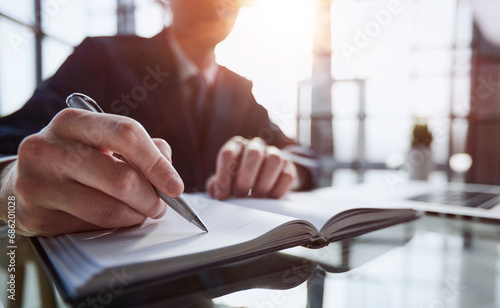 Close up of woman's hands writing in spiral notepad placed on wooden desktop with various items