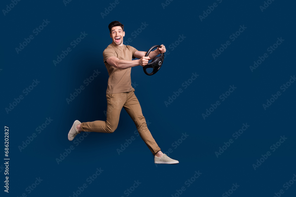 Obraz premium Full size photo of impressed ecstatic man wear beige outfit running with steering wheel in hands isolated on dark blue color background