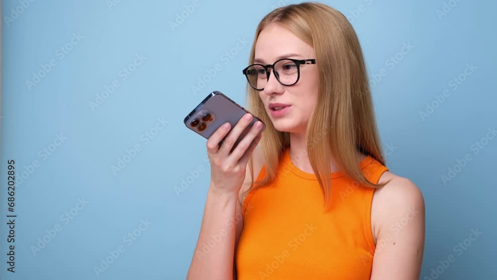 Young woman with glasses looking at her phone on blue background. Portrait of a young woman talking to her phone on a monochrome background with space for text Young woman with glasses looking at her phone on blue background. Portrait of a young woman talking to her phone on a monochrome background with space for text