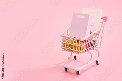 Annual sale shopping season concept - mini pink shop cart trolley full of paper bag gift isolated on pale pink background, blank copy space, close up