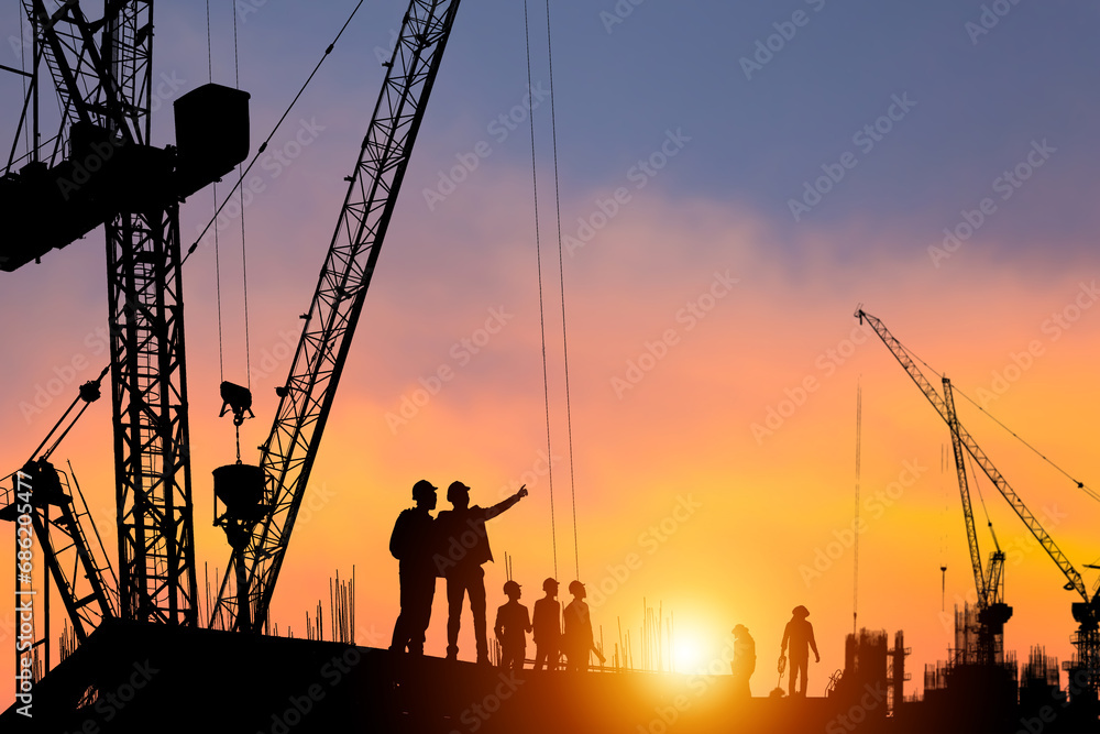 Silhouette of Engineer and worker checking project at construction site, building site with blurred sunset sky in evening time background