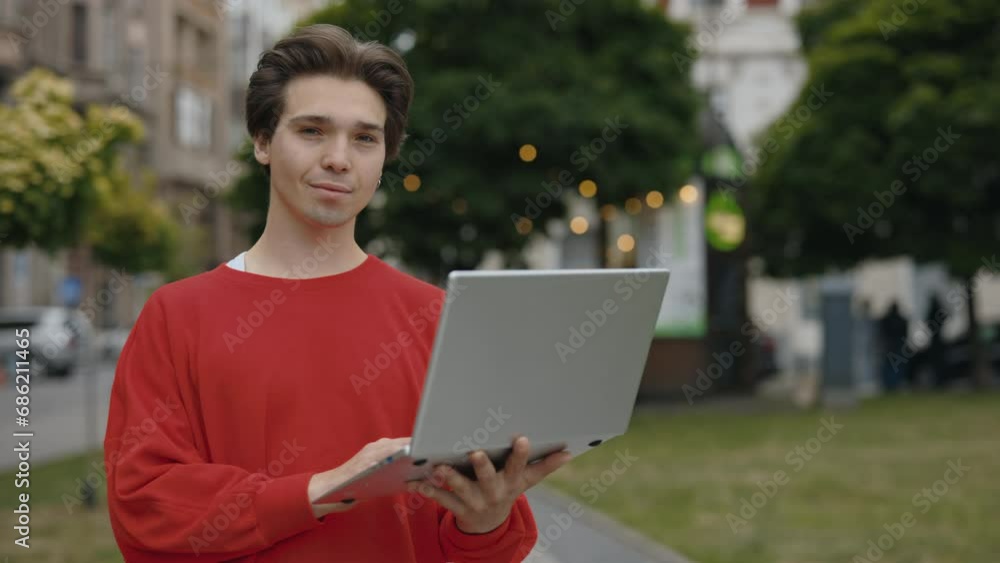 Handsome Caucasian man standing on the street, utilizing a laptop. A male professional working outdoors with his computer. Portrait of guy looking at camera Handsome Caucasian man standing on the street, utilizing a laptop. A male professional working outdoors with his computer. Portrait of guy looking at camera
