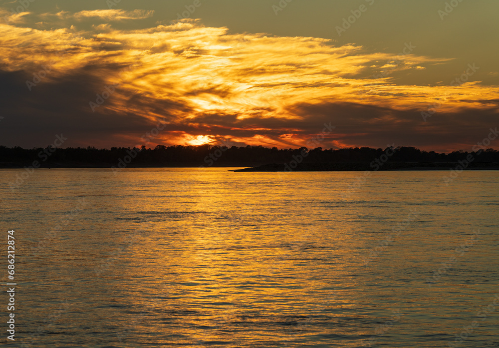 Clouds hide setting sun giving golden glow across the calm Mississippi River in Missouri