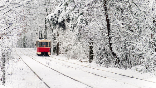 Red tram moving on the rails in the winter snowy forest. Selective focus.