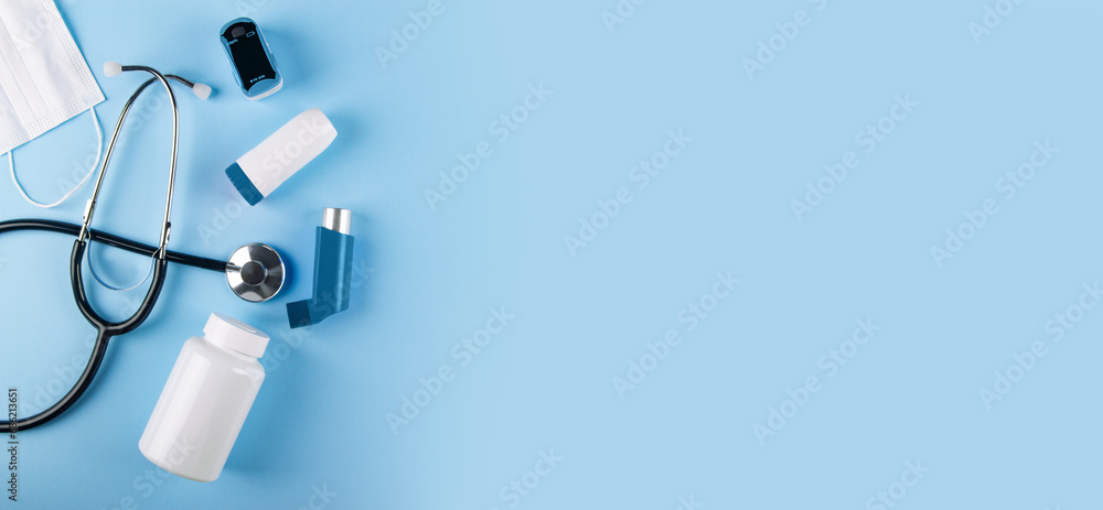 Top view of medical mask, stethoscope, oximeter, bottle of pills and inhalers on blue background with copy space. Banner for Allergy-induced asthma concept Top view of medical mask, stethoscope, oximeter, bottle of pills and inhalers on blue background with copy space. Banner for Allergy-induced asthma concept