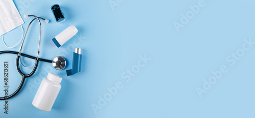 Top view of medical mask, stethoscope, oximeter, bottle of pills and inhalers on blue background with copy space. Banner for Allergy-induced asthma concept photo