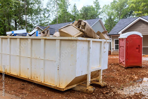 Dumpster full of construction waste debris is positioned near construction site.