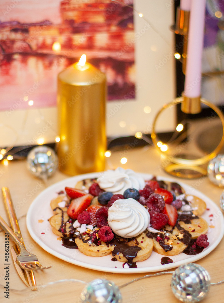 Viennese waffles with berries on a wooden table, breakfast, no people. Festive dessert, candles and string lights on the background