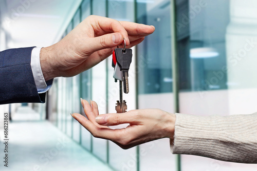 Real estate concept. Estate agent giving house keys against abstract modern office building background