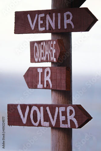 quatro setas de madeira presas a um poste indicando caminhos simbólicos ou escolhas onde se le em espanhol: venir, quedarse, ir, volver photo