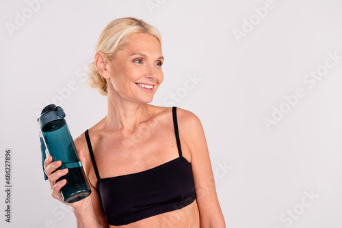 Photo of lovely cheerful person toothy smile hand hold bottle water look empty space isolated on grey color background