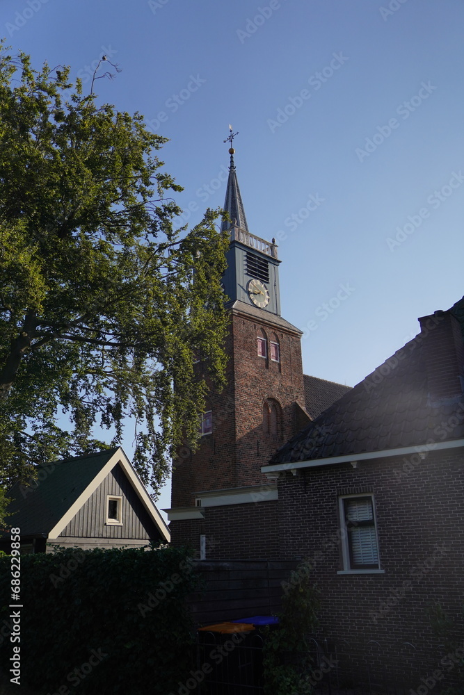 The historic church steeple rises elegantly over a small Dutch town, marking time with its timeless clock face The historic church steeple rises elegantly over a small Dutch town, marking time with its timeless clock face