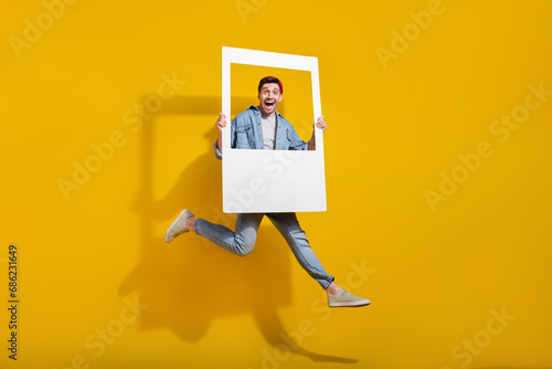 Full length photo of good mood positive guy wear denim jacket rising photo frame jumping high isolated yellow color background