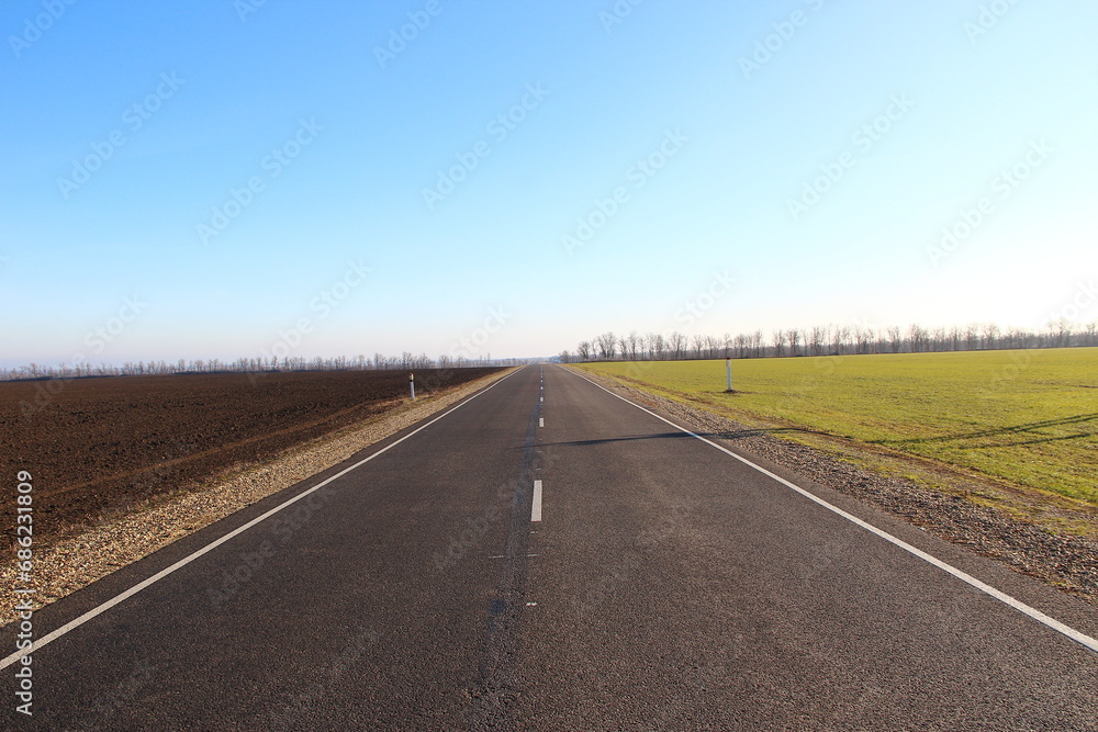 Asphalt road near agricultural fields and blue sky on a backround