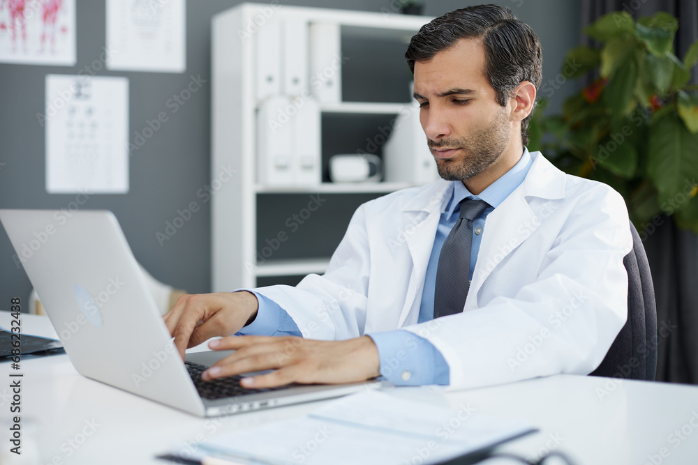 Focused doctor sitting at his desk using his laptop