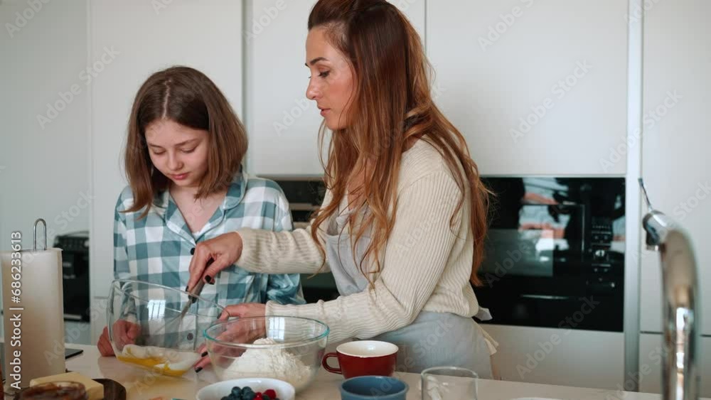 Cheerful mom and daughter whipping eggs and flour and talking while making breakfast in kitchen Cheerful mom and daughter whipping eggs and flour and talking while making breakfast in kitchen