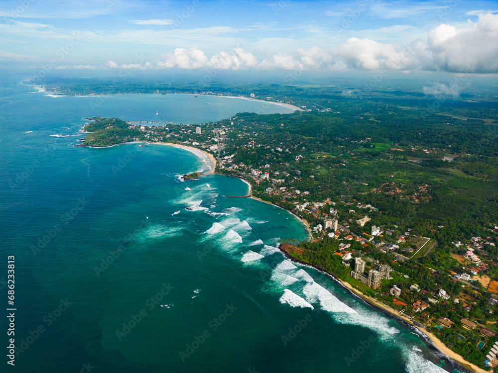 Aerial view with panoramic coastline with sparkling turquoise waters against a lush green landscape, showcasing scenic coastal living and the junction between land and sea from birds-eye perspective.