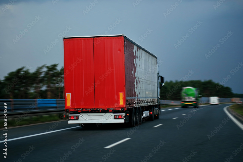 Modern Semi-Trailer Trucks On The Highway Driving In The Right Lane. Commercial Vehicle For Shipping And Post Delivery. Shipping Of The Goods On Land Door-To-Door Modern Semi-Trailer Trucks On The Highway Driving In The Right Lane. Commercial Vehicle For Shipping And Post Delivery. Shipping Of The Goods On Land Door-To-Door