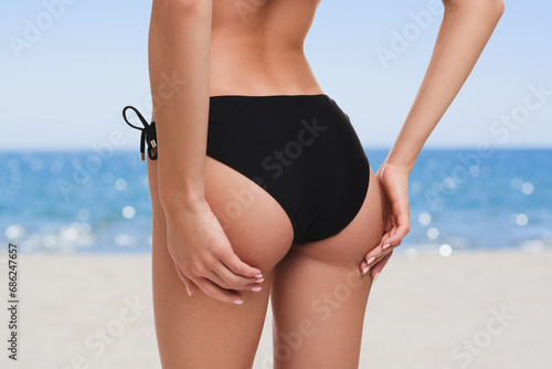 Woman in stylish black bikini on sandy beach near sea, closeup