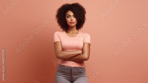 Confident black woman stands with crossed arms against soothing solid beige pink backdrop symbolizing resilience elegance and self assurance, crossed arms reflecting blend of grace and determination