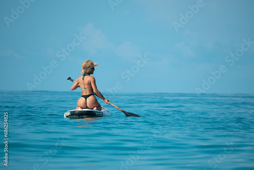 sexy girl in a swimsuit on a sup board lies resting on a board under the bright sun on the background of the sea , Stand up paddleboarding