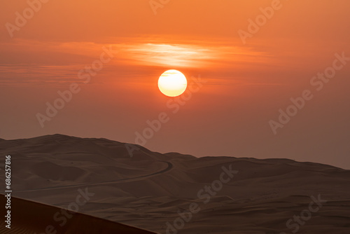 Sunrise over the sand dunes with an empty road in the horizon, hazy sky.