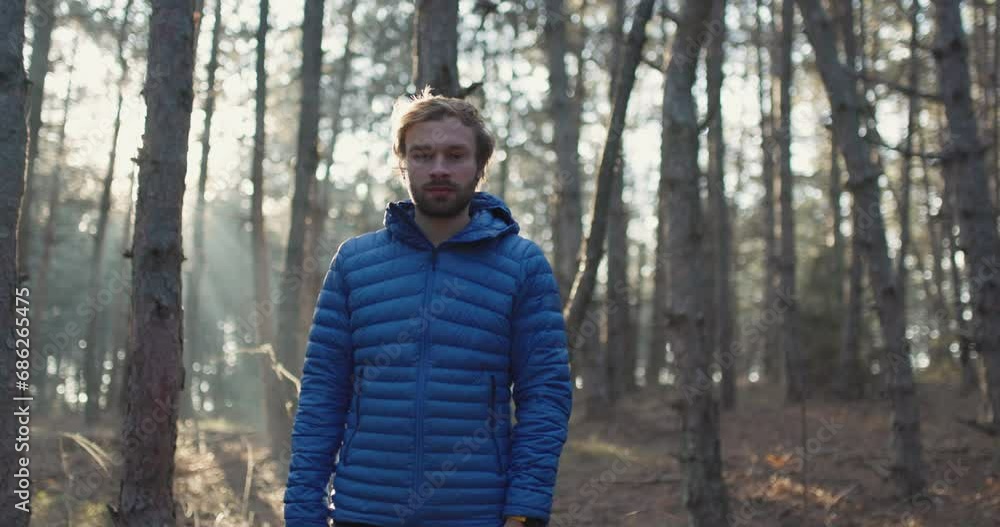 Portrait of a trail runner man standing in the woods. Sun shining through trees in a forest on sunset. Slowmotion video.