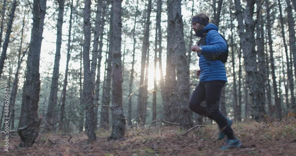 Trail runner in the woods wearing winter sports outfit. Man running on a forest path. Sun shining between trees. Recorded at 120 fps. Trail runner in the woods wearing winter sports outfit. Man running on a forest path. Sun shining between trees. Recorded at 120 fps.