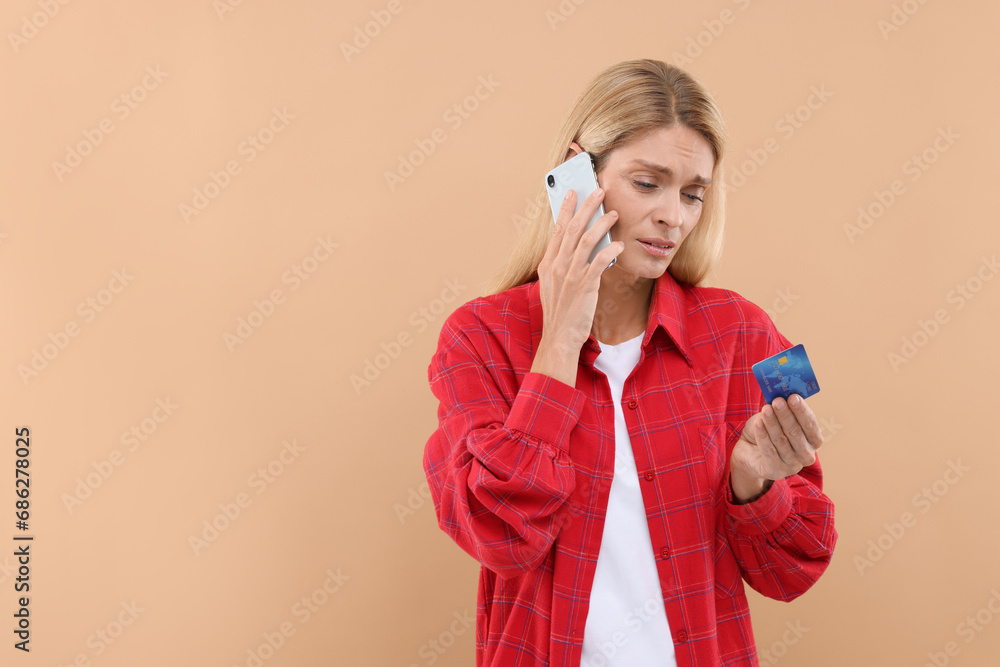 Stressed woman with credit card talking on smartphone against beige background, space for text. Be careful - fraud Stressed woman with credit card talking on smartphone against beige background, space for text. Be careful - fraud