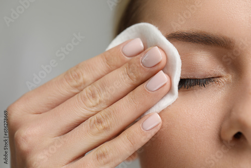 Woman removing makeup with cotton pad on grey background, closeup photo