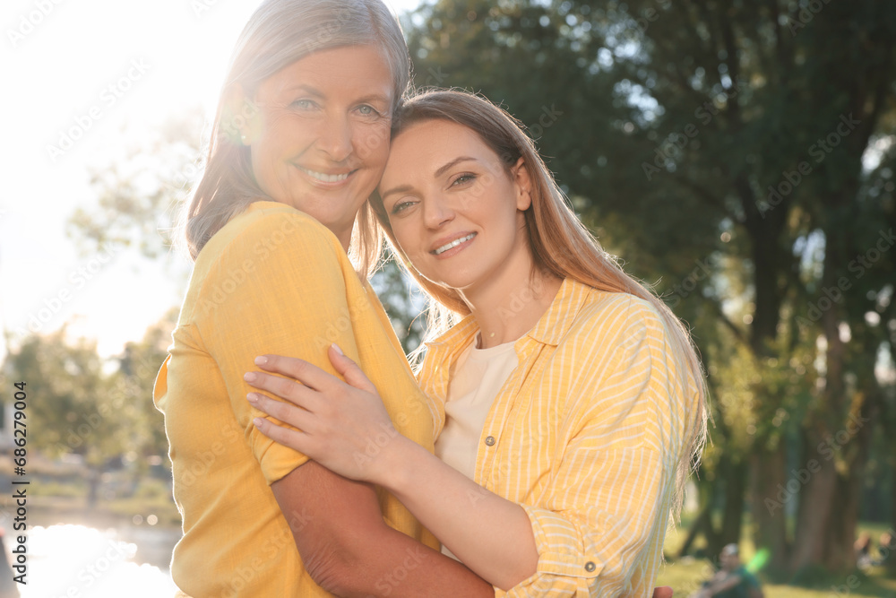Family portrait of happy mother and daughter hugging outdoors on sunny day
