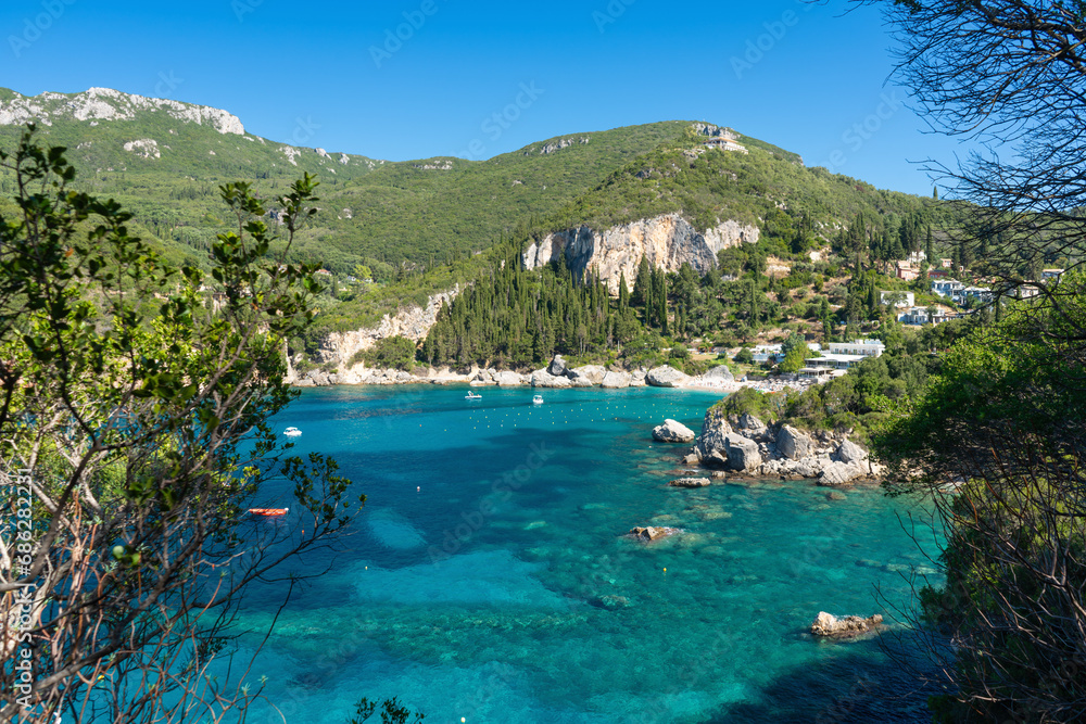Sun shines to calm blue sea at Liapades bay, view from small rocky cliff near, green coniferous trees and bushes in foreground