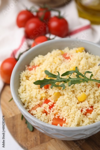 Tasty couscous with pepper, corn and arugula in bowl on white table, closeup