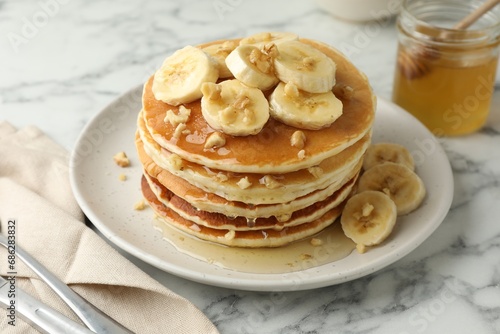 Delicious pancakes with bananas, walnuts and honey on white marble table, closeup