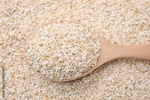 Wooden spoon on raw barley groats, top view