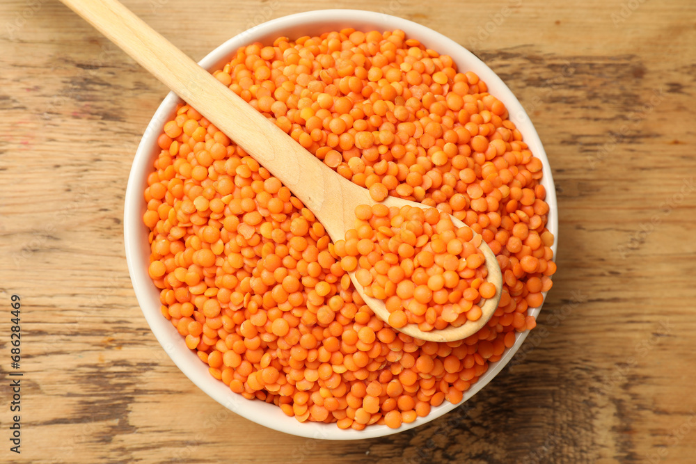 Raw red lentils in bowl and spoon on wooden table, top view Raw red lentils in bowl and spoon on wooden table, top view