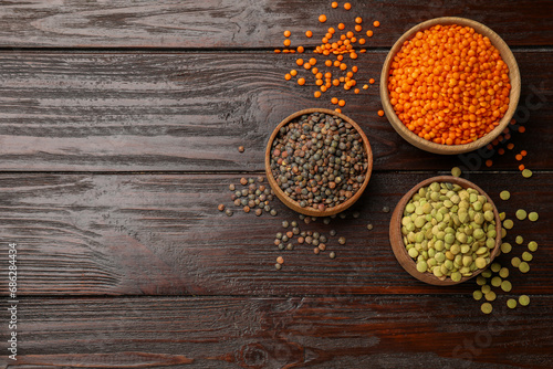 Different types of lentils in bowls on wooden table, flat lay. Space for text