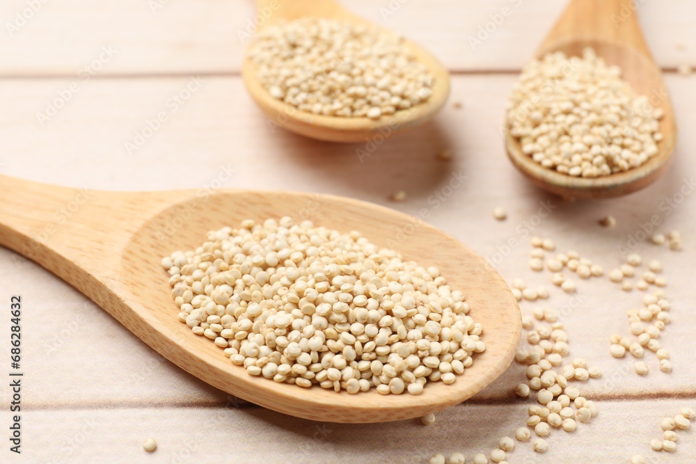 Spoons with raw quinoa on wooden table, closeup Spoons with raw quinoa on wooden table, closeup