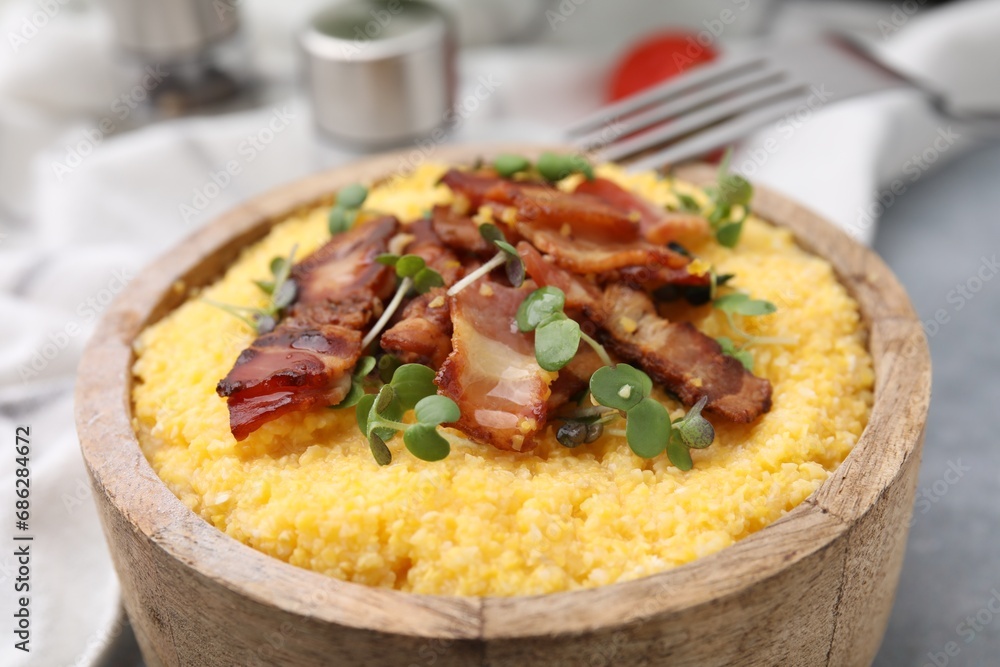 Cooked cornmeal with bacon and microgreens in bowl on light table, closeup Cooked cornmeal with bacon and microgreens in bowl on light table, closeup